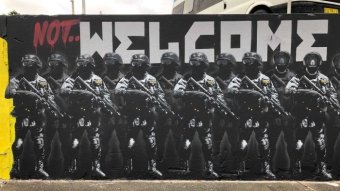 A mural reading 'not welcome', depicting a line of thuggish-looking riot cops.