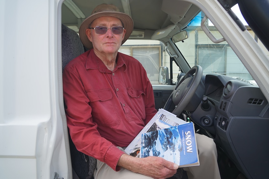 An older man with a hat and glasses on looks into the distance.