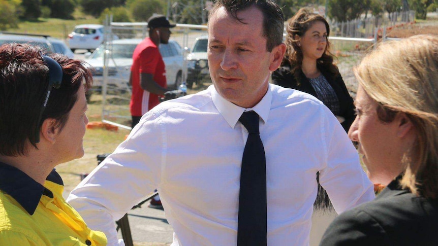 A mid-shot of Mark McGowan in a white shirt and dark tie talking to two women.