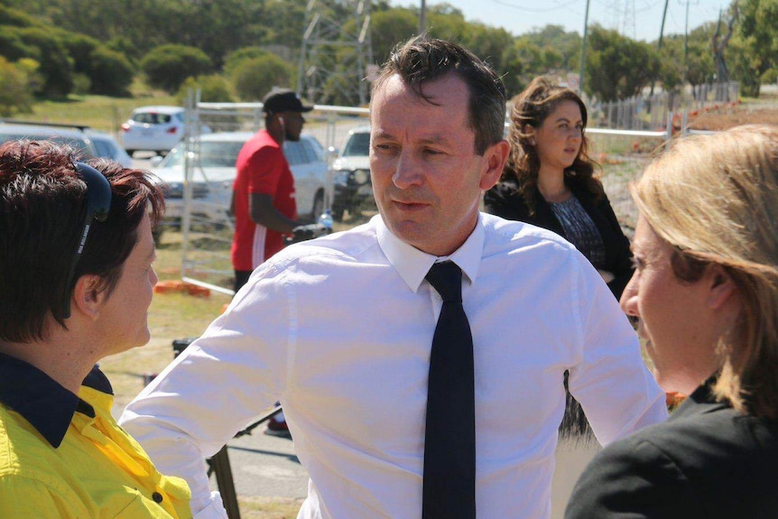 A mid-shot of Mark McGowan in a white shirt and dark tie talking to two women.