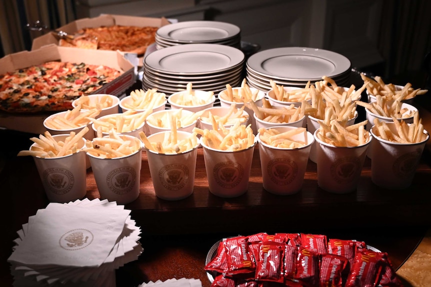French fries, in white containers carrying the Presidential seal, and pizza are presented on a table at the White House.