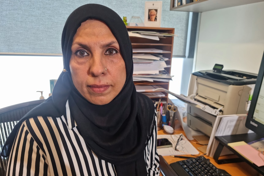 A woman in a black hijab sits in a doctor's office looking serious.