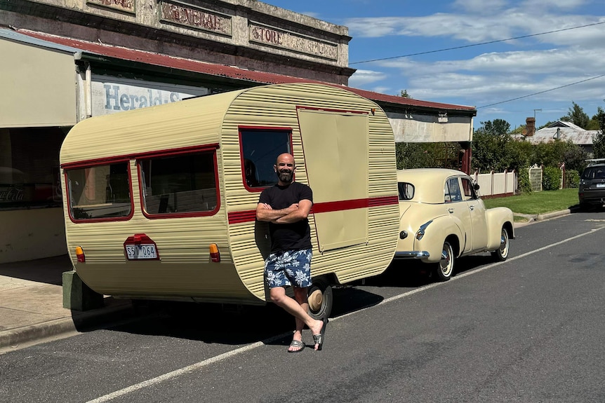 A man crossing his arms and leaning against his caravan. 