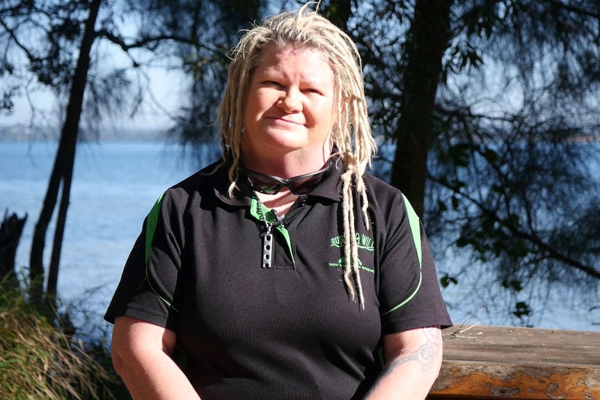 Youth worker Julie Larson  stands outside on Macleay Island off Brisbane with the ocean behind her.