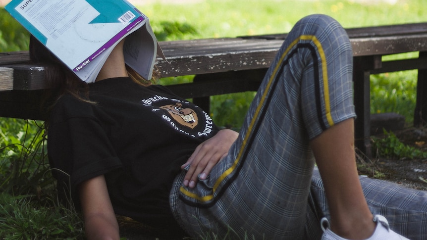 woman lying down on the grass with a book covering her face