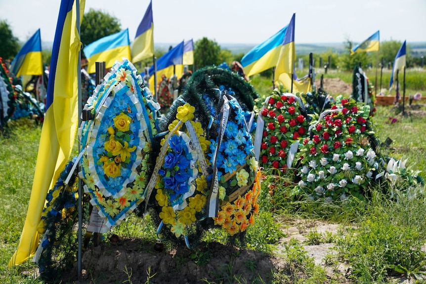 Flags and flowers on several graves in a cemetary.