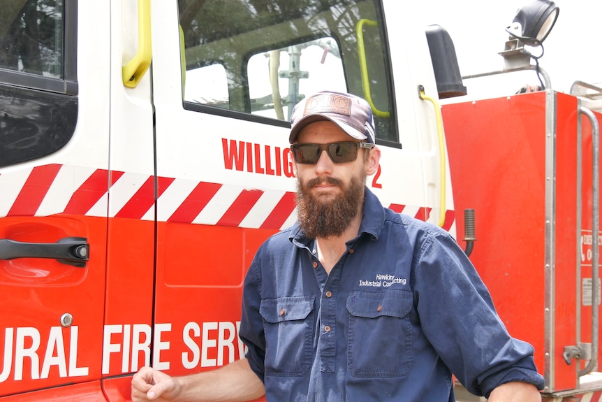 a man with a hat and sunglasses on posing in front of a striped firetruck.