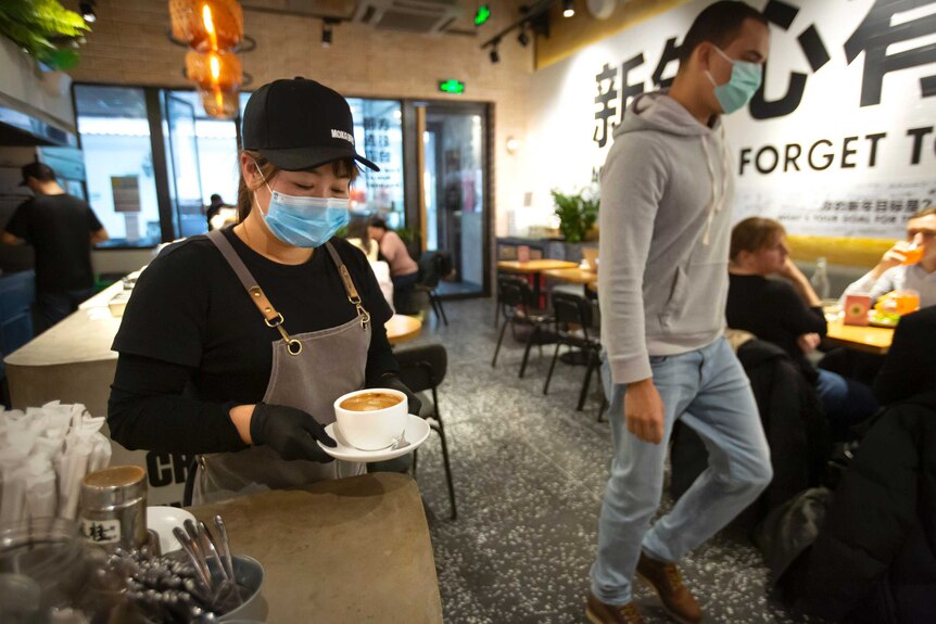 A server wearing a face mask carries a cup of coffee at a cafe in Beijing.