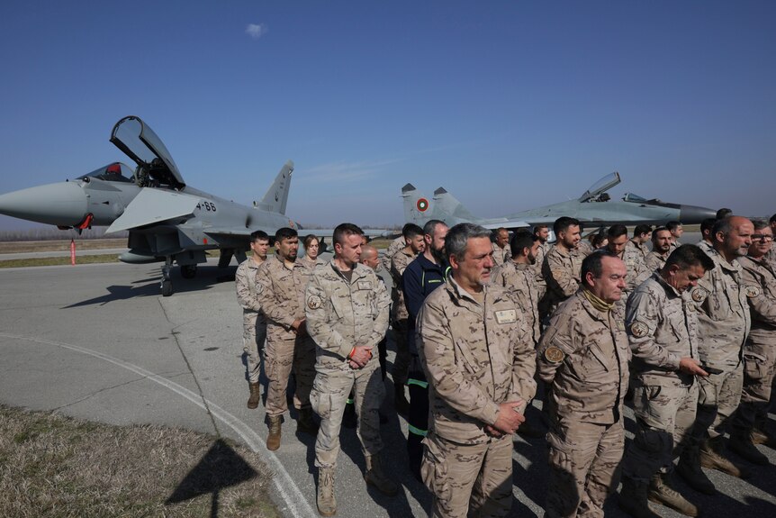 Soldiers stand in front of two military planes.