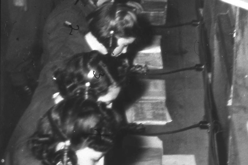 Black and white photo of female wireless operators, working and sitting side by side at a long desk
