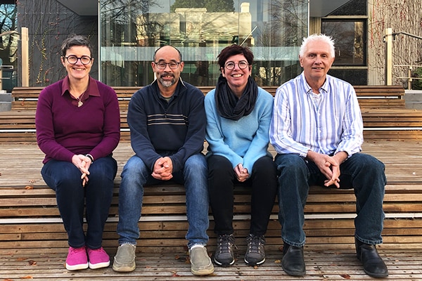 Four academics sit on a step and smile at the camera