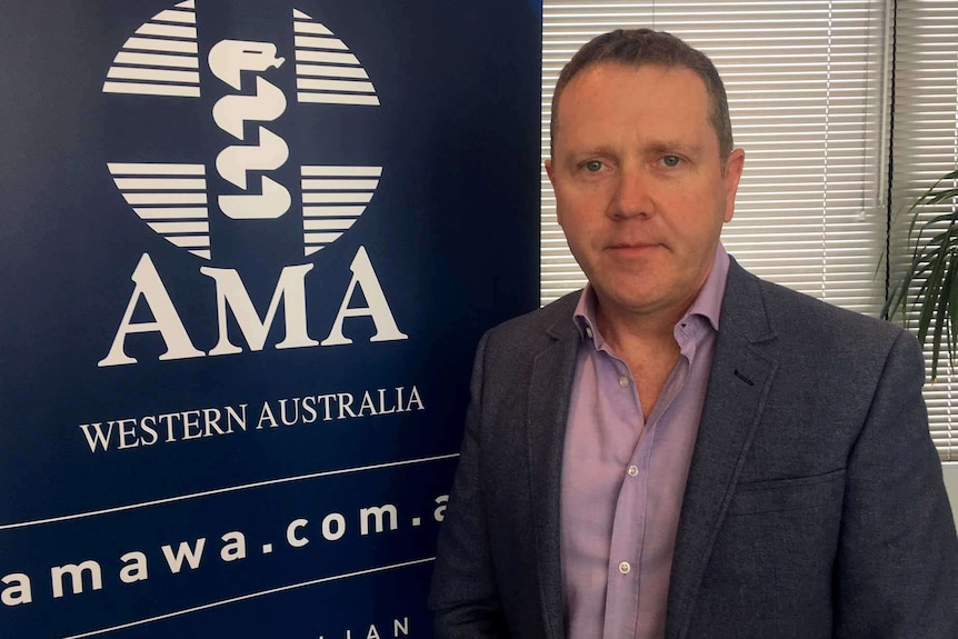 A man in an open-necked shirt and suit jacket stands in front of an AMA sign