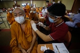 A Buddhist monk in orange robes receives a coronavirus vaccine