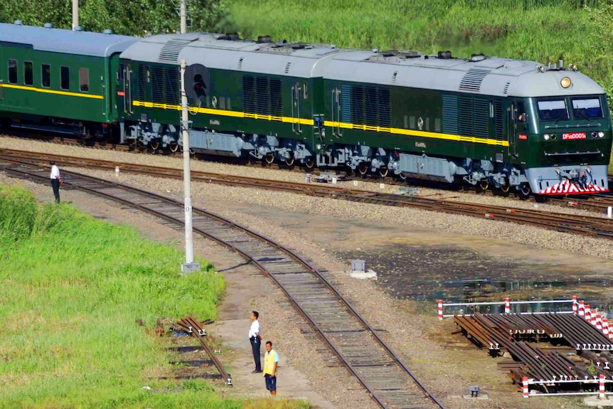 A green armored train travelling on a track through green fields in China