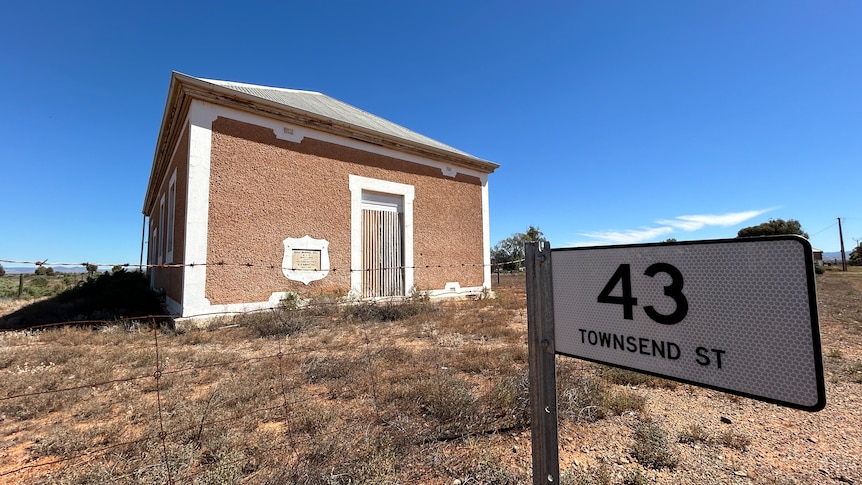 An old memorial hall stands in the country with a bright blue sky, with street sign in the foreground.
