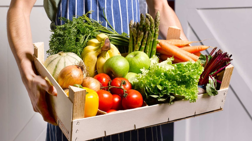 person carrying a wooden tray of fresh vegetables