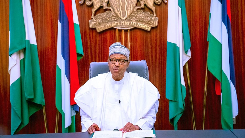 Nigeria's President Muhammadu Buhari addresses the nation on a live televised broadcast in front of flags.