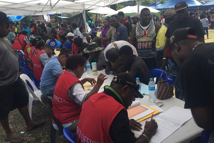 People lining up to enrol to vote at a stall set up outdoors.