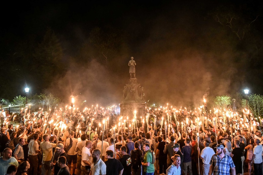 A group of white men with lit tiki torches surrounding a statue of Robert E Lee