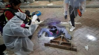 A person climbs down into a manhole to escape police as others watch.