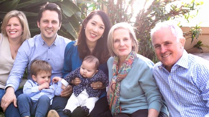 Malcolm Turnbull sits on the grass with wife, his adult children and their partners, and two babies, smiling at the camera