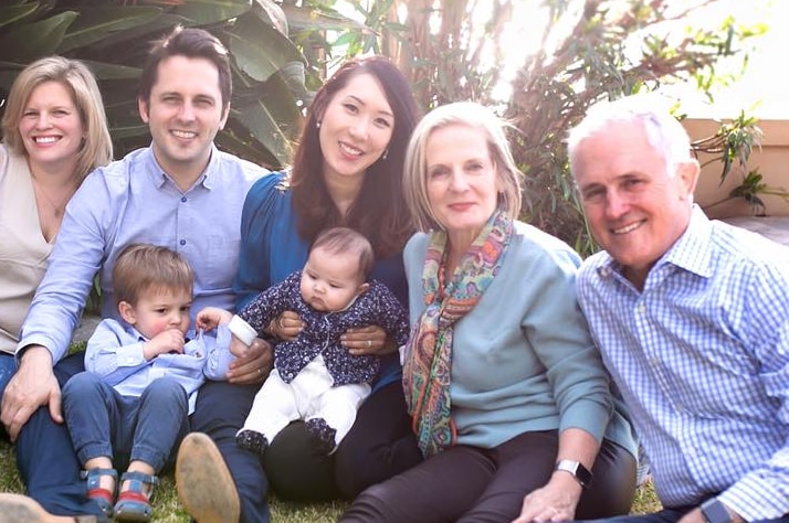 Malcolm Turnbull sits on the grass with wife, his adult children and their partners, and two babies, smiling at the camera
