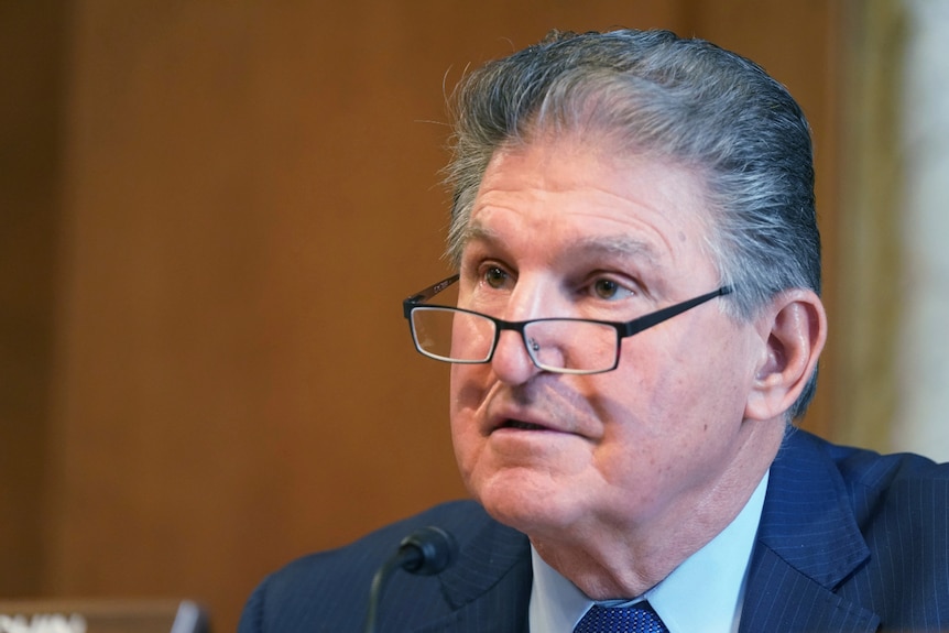 Joe Manchin looking left of image wearing glasses perched on the end of his nose