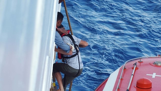 One man is climbing up a ladder on the side of a ship from a rescue boat