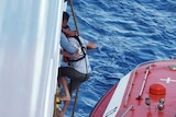 One man is climbing up a ladder on the side of a ship from a rescue boat