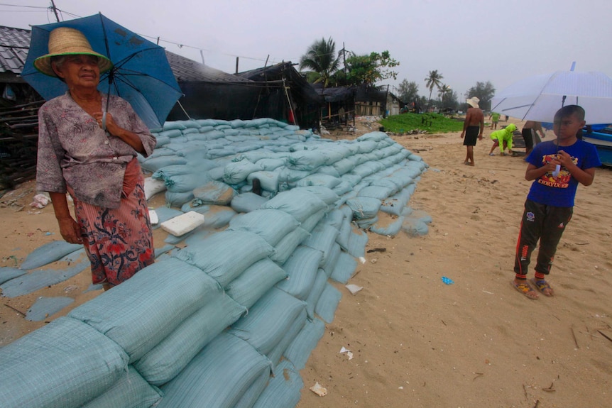 A Thai woman stands behind sandbags on a beach.