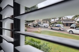 Taken through window shutters, a person is arrested on a suburban street by many police officers