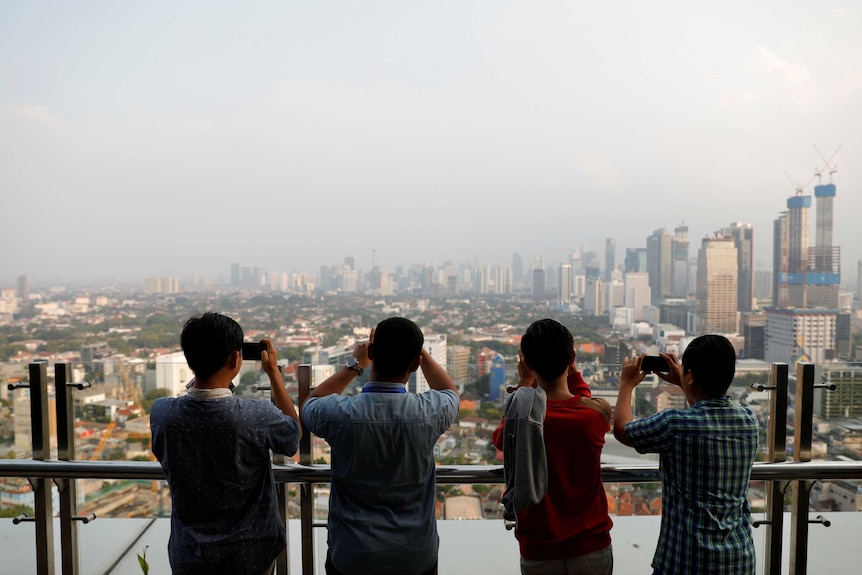 A row of men taking photos of a smoggy Jakarta skyline
