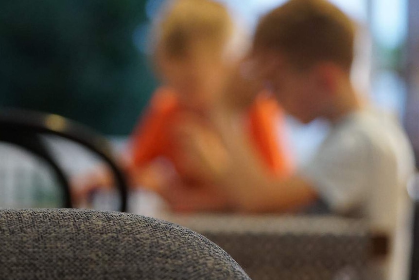 Two anonymous primary school-aged boys sit at a table in a house in Australia.