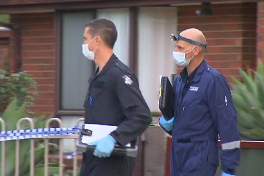 Two forensic police officers arrive at a house which has been fenced off with police tape.