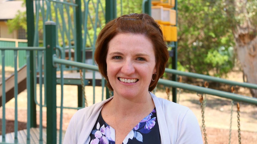 A woman with short brown hair stands in front of a children's playground