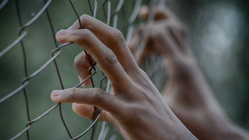 Close up of a young person's hands gripping a wire fence