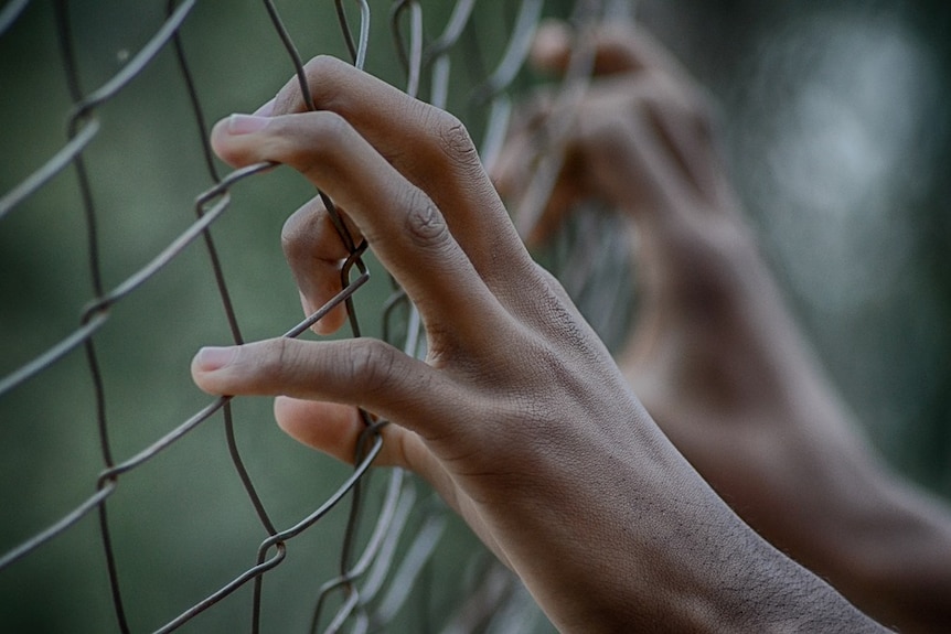 Close up of a young person's hands gripping a wire fence