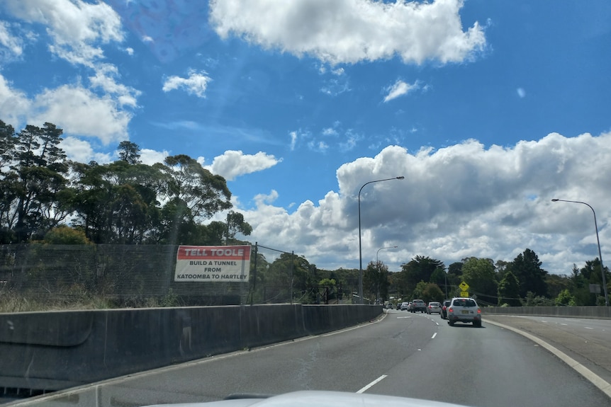 A sign next to a road calls for a tunnel to be drilled between Katoomba and Lithgow.