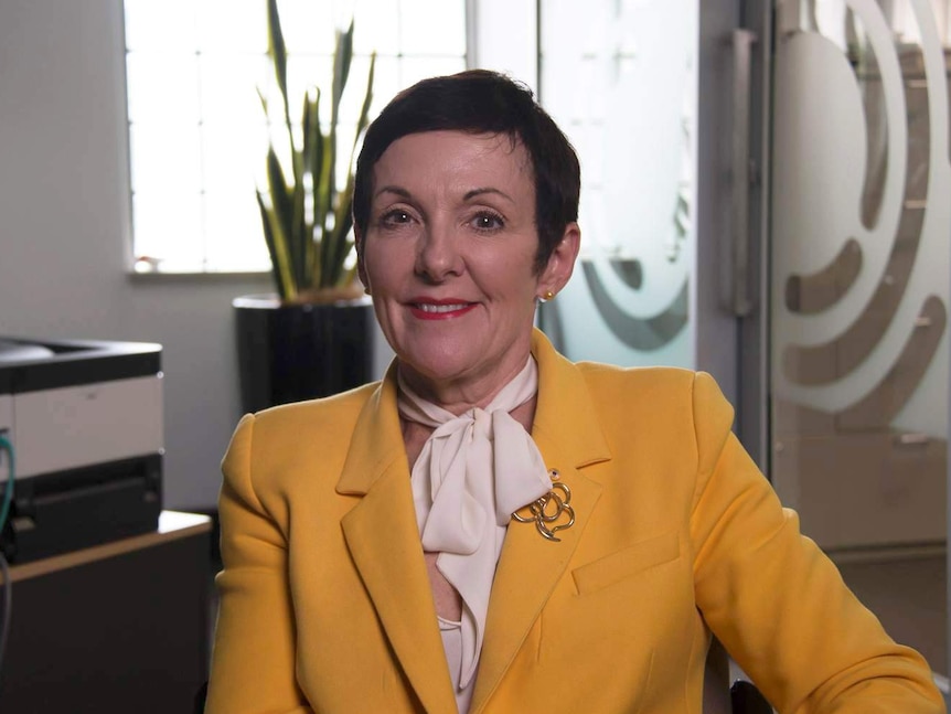 Kate Carnell wears a yellow blazer and sits smiling into the camera.