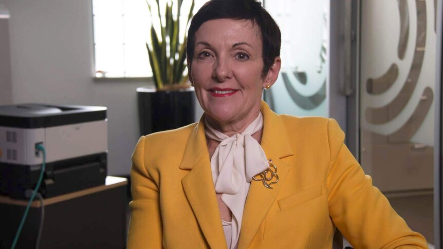 Kate Carnell wears a yellow blazer and sits smiling into the camera.