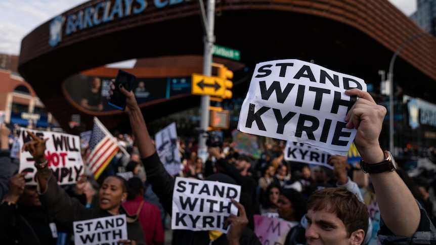Protesters holding up signs that say "stand with Kyrie" out the front of a basketball stadium