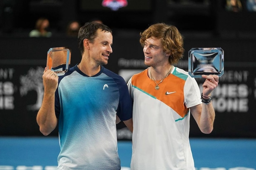 Denys Molchanov and Andrey Rublev look at each other while holding their silver Marseille Open doubles trophies.