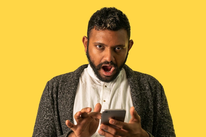 Photo of Shahmen Suku holding a phone on a yellow background. He's faced racism on gay dating apps like Grindr.