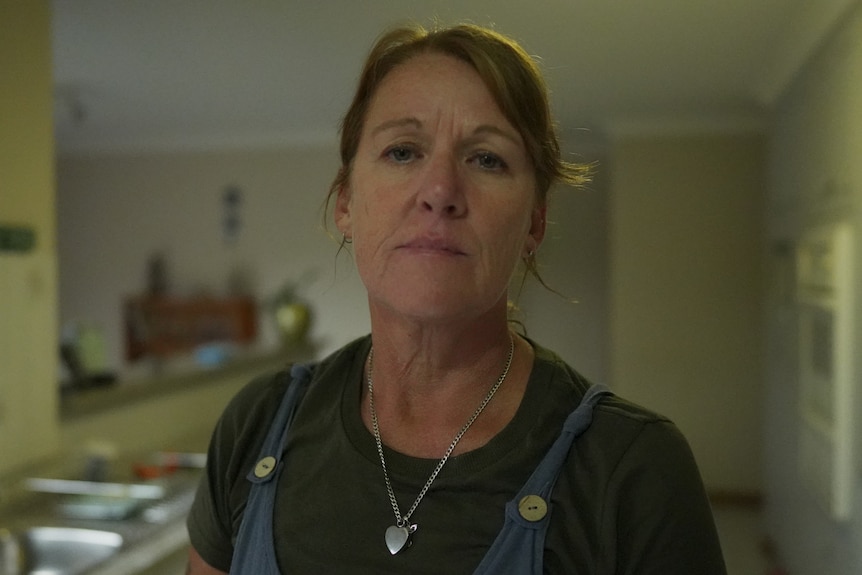 A woman stands in her kitchen, with a serious expression on her face.