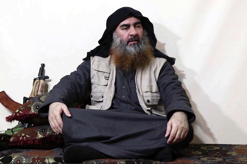 Abu Bakr al-Baghdadi sits cross-legged next to an AK-47 gun.