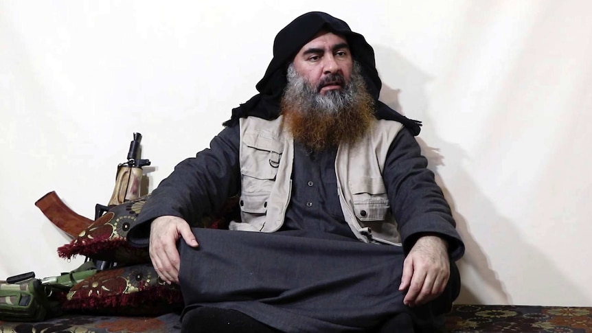 Abu Bakr al-Baghdadi sits cross-legged next to an AK-47 gun.