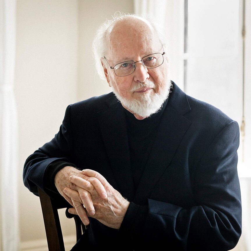 A photograph of film composer John Williams, wearing a dark suit against a light background.