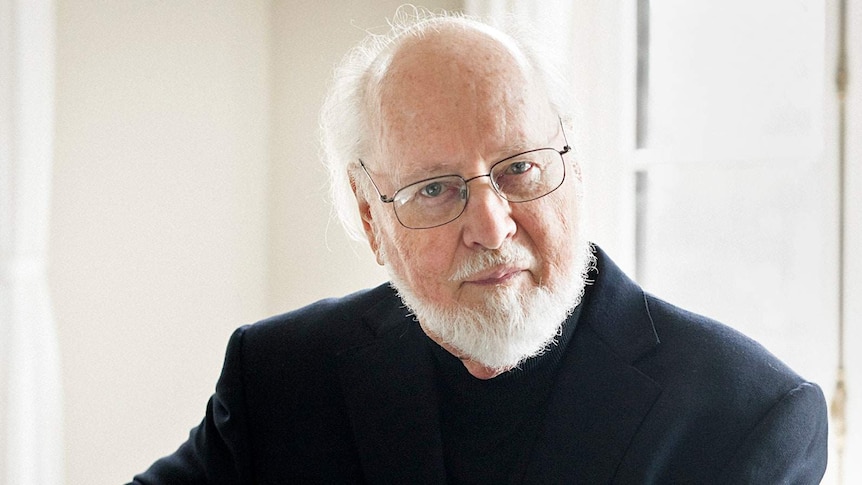 A photograph of film composer John Williams, wearing a dark suit against a light background.