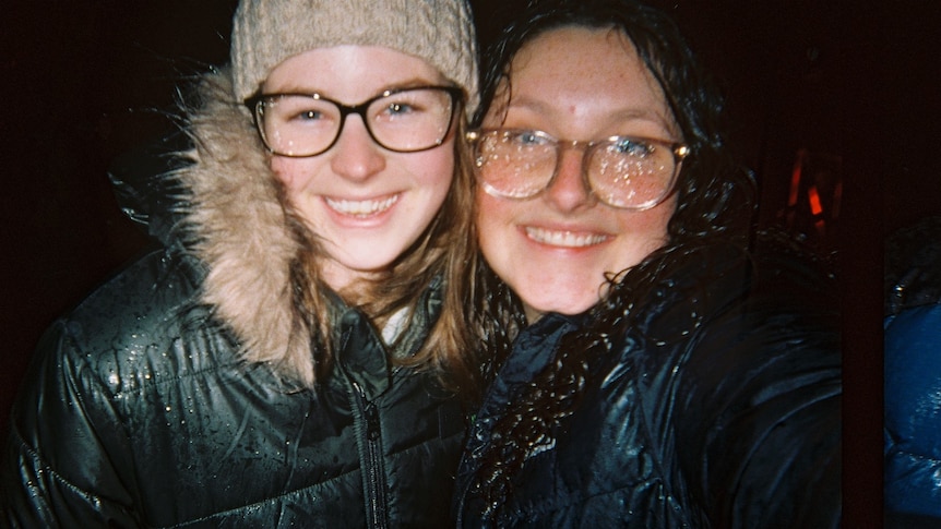 Jamison and a friend smile at the camera at night in the rain