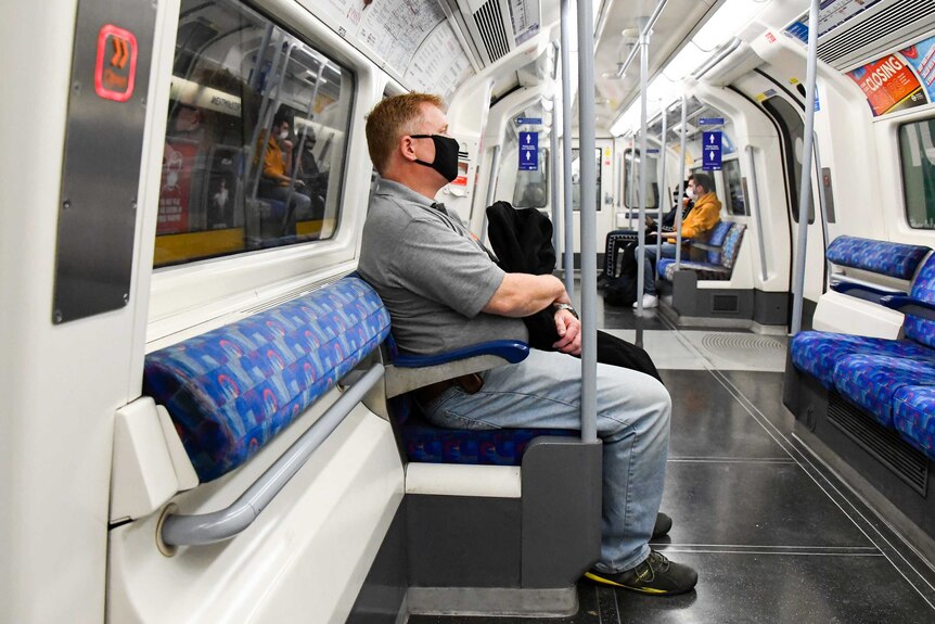 A man wears a face mask while sitting far from the other few passengers on an Underground train.